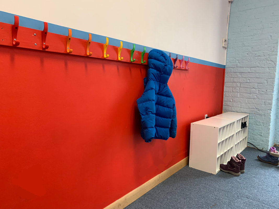 Plastic hooks in colors red through purple on a red wall with a blue coat hanging on a hook