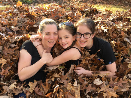 Master Giletti in a pile of leaves with her two daughters